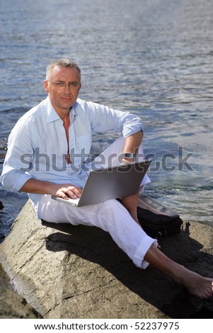 Man sitting on a rock with a laptop computer at the sea