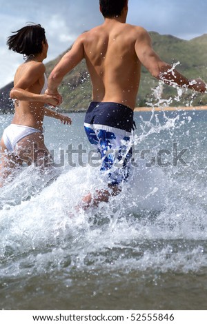 A man and a woman running in the water seen from the back