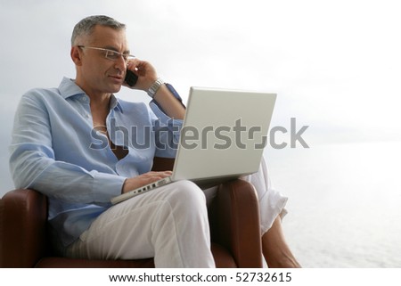Man sitting in an armchair with a laptop computer and a phone