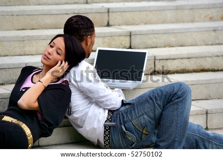 Portrait of a young smiling woman phoning and a young man in front of a laptop computer