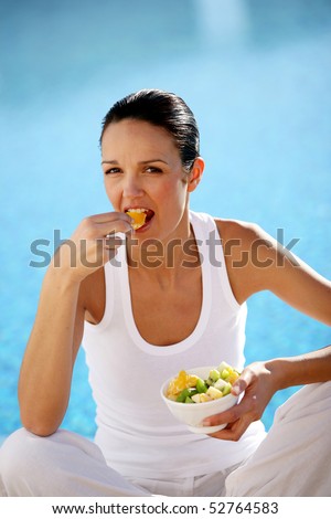 Smiling woman eating a salad of fruits next to a swimming pool