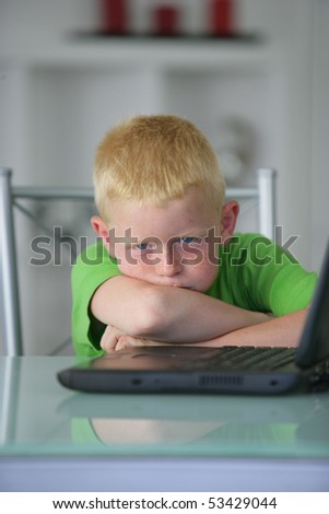 Portrait of an angry little boy in front of a laptop computer