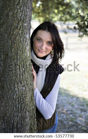 Portrait of a smiling young woman hidden behind a tree