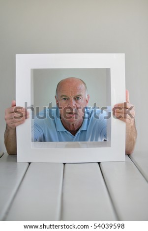 Portrait of a senior man with a look of surprise behind a white frame