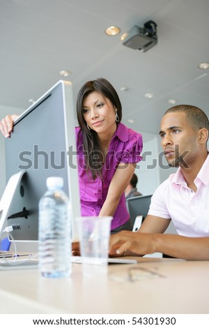 Portrait of a young woman and a young man in front of a desktop computer