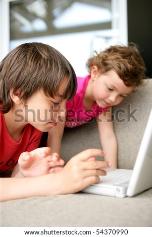 Portrait of a little boy and a little girl on a sofa in front of a laptop computer
