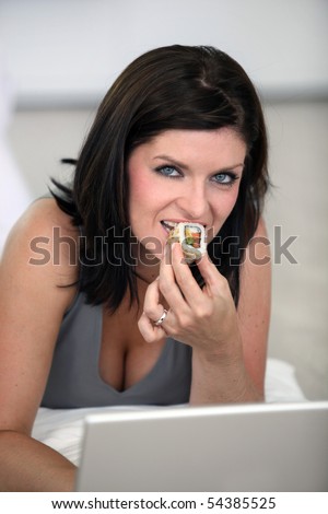 Portrait of a young woman eating sushi in front of a laptop computer