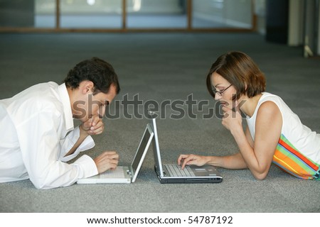 A man and a woman lying on the floor with laptop computers face to face