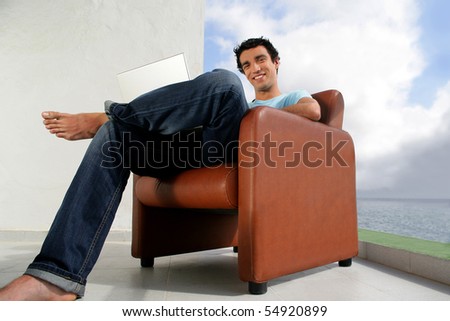 Portrait of a young man sitting in an armchair in front of a laptop computer