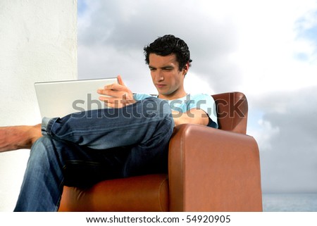 Portrait of a young man sitting in an armchair in front of a laptop computer