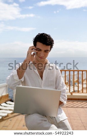 Portrait of a young man phoning in front of a laptop computer