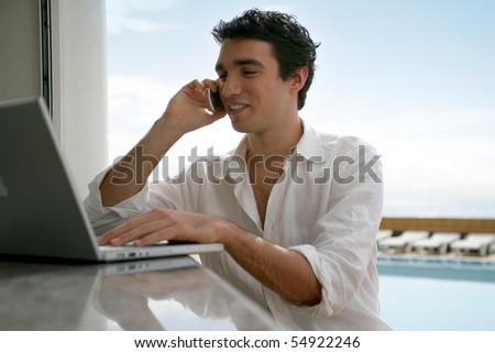 Portrait of a young man phoning in front of a laptop computer