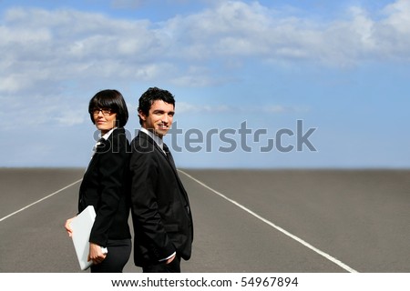 Portrait of a man and a woman in suit back to back with a laptop computer