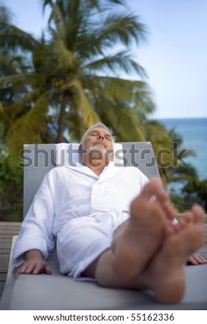 Senior man in bathrobe lying on a deck chair