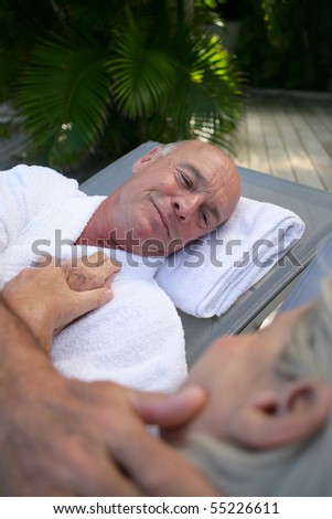 Portrait of a senior man in bathrobe lying on a deck chair face to a senior woman