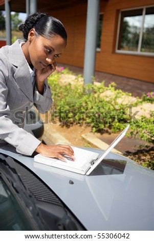 Young woman in suit phoning with a laptop computer placed on a car