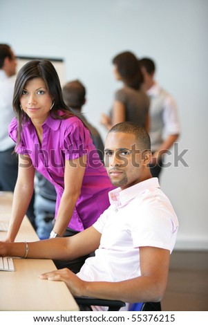 Portrait of a young woman and a young man sitting in front of a desktop computer