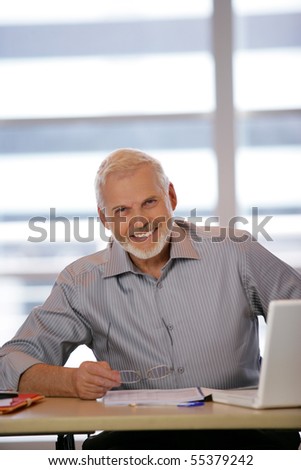 Portrait of a senior man sitting at a desk in front of a laptop computer