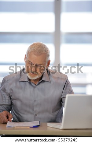 Portrait of a senior man sitting at a desk in front of a laptop computer