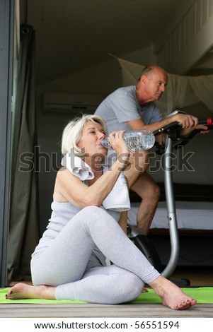 Elderly woman drinking water after exercise near a man doing bike