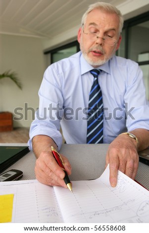 Senior man sitting at a desk writing on his diary