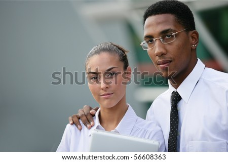 Portrait of a young man in suit near a young woman in suit holding a laptop computer