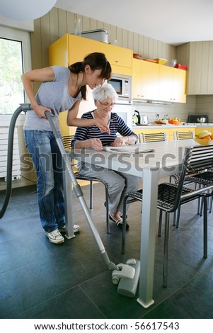 Young woman vacuuming near a senior woman reading the newspaper