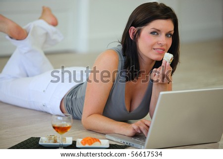 Portrait of a woman laid on the floor eating a sushi in front of a laptop computer