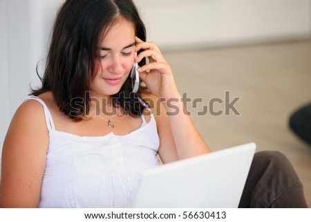 Portrait of a young girl phoning in front of a laptop computer