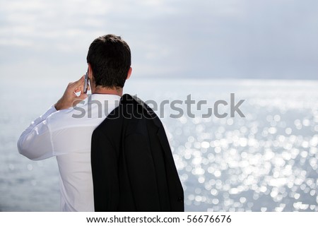 Young man in suit with a phone face to the sea