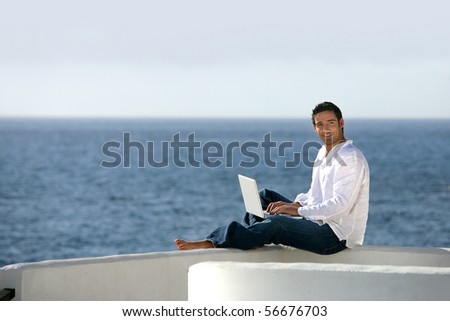 Young man sitting in front of a laptop computer face to the sea