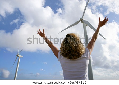 Young woman with arms up face to a wind turbine