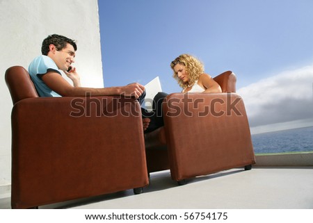 Young man phoning in front of a young woman with a laptop computer