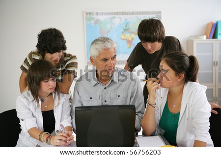 Portrait of a man and a group of teenagers in front of a laptop computer in a classroom