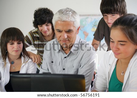 Portrait of a man and a group of teenagers in front of a laptop computer in a classroom
