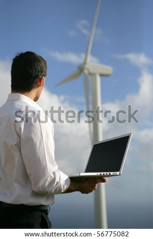 Young man in suit with a laptop computer face to a wind turbine
