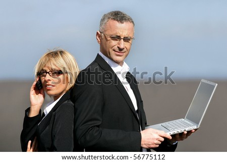 Man in suit with a laptop computer back to back with a woman in suit phoning