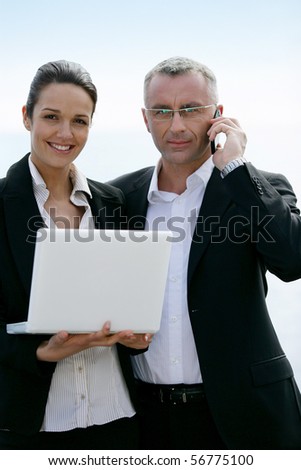 Man in suit phoning near a woman in a woman in suit with a laptop computer