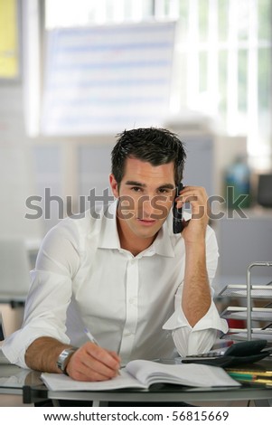 Portrait of a young man sitting at a desk phoning and writing on a document