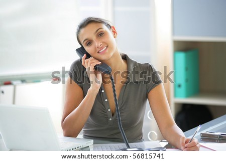 Portrait of a smiling woman on the phone at desk