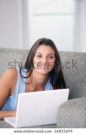 Portrait of a smiling young woman laid on a sofa in front of a laptop computer