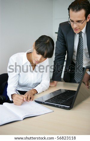 Portrait of a young man and a young woman writing on a document in front of a laptop computer