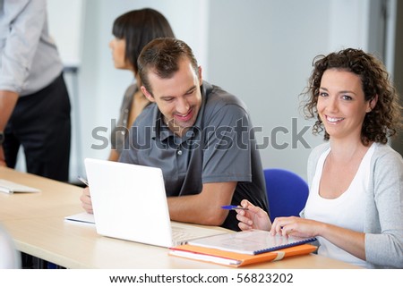 Portrait of a young man and a young woman smiling sitting at a desk in front of a laptop computer