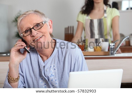 Senior woman phoning in front of a laptop computer