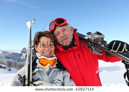 Portrait of a senior man and a senior woman smiling with skis in snow