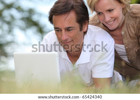 Man and woman laid in the grass in front of a laptop computer