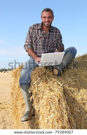 farmer seated on straw bale and doing computer