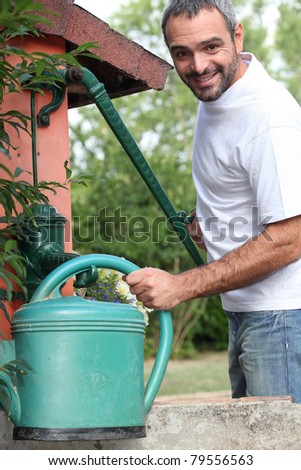 a mid aged man filling a  watering can with a cast iron water pump