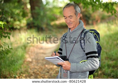 sixty years old man taking notes on a forest trail