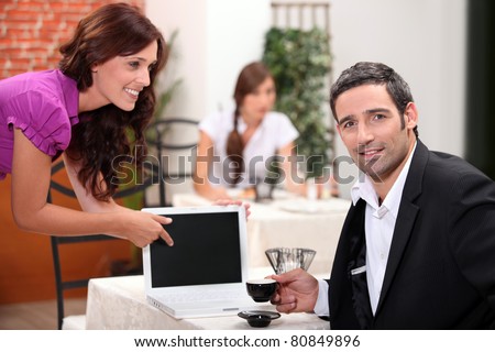 Woman in a restaurant pointing to a computer screen left blank for your image